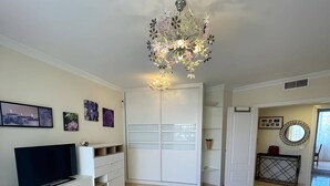 Un salon moderne avec un canapé beige, un meuble de télévision blanc, un téléviseur à écran plat, une table basse ronde et un lustre décoratif.