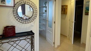 Un couloir doté d’un sol carrelé, d’un miroir rond au cadre métallique et d’un sac rouge posé sur une console.