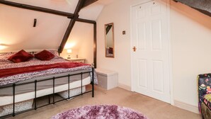 Ein Schlafzimmer mit schrägverdeckter Decke, einem Bett mit gemustertem Bettbezug, einem Nachttisch mit Lampe, einem Spiegel an der Wand und einer weißen Tür.
