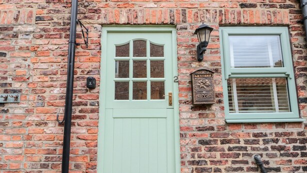Ein Backsteinhaus mit grüner Tür, einem Fenster mit Rollo und einem Briefkasten an der Wand.