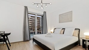 Une chambre moderne avec un grand lit, un bureau et une vue sur le paysage urbain par la fenêtre.