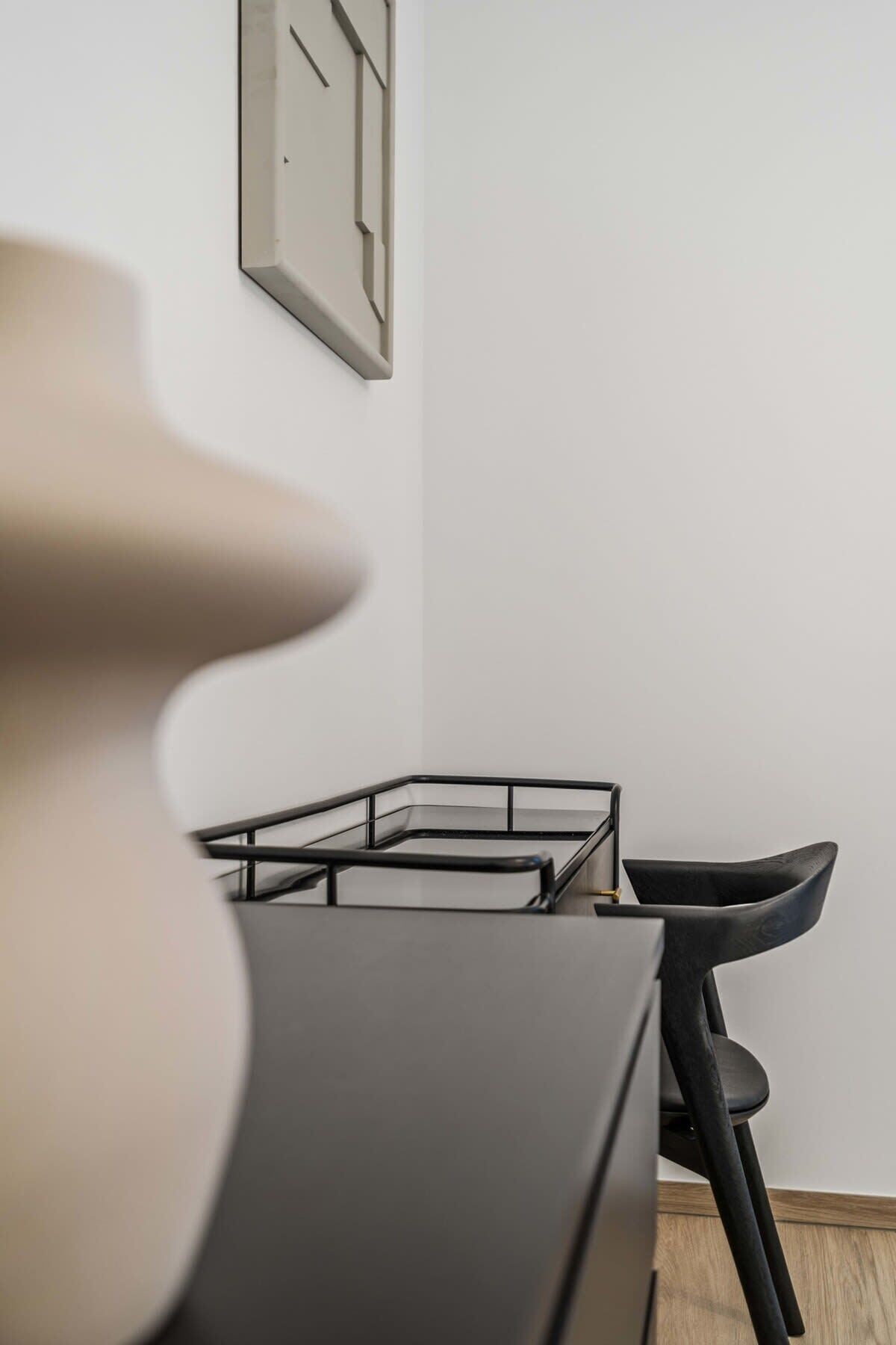 Une pièce moderne et minimaliste, avec une table à plateau de verre, une chaise noire et un tableau encadré accroché au mur.