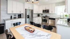 A modern kitchen with white cabinets, stainless steel appliances, a marble countertop, and a dining area with a wooden table and chairs.