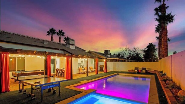 A pool area with a table tennis table and chairs, a pool with illuminated blue lighting, and a covered seating area with red curtains.