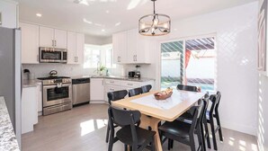 A modern kitchen with white cabinets, stainless steel appliances, and a dining area with black chairs and a wooden table.