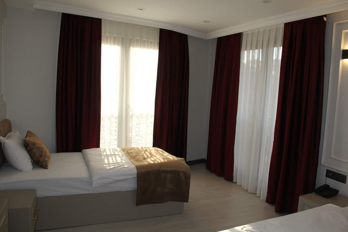 A hotel room with a bed, a bedside table, and a window with curtains.