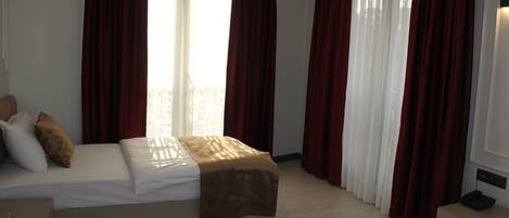 A hotel room with a bed, a bedside table, and a window with curtains.