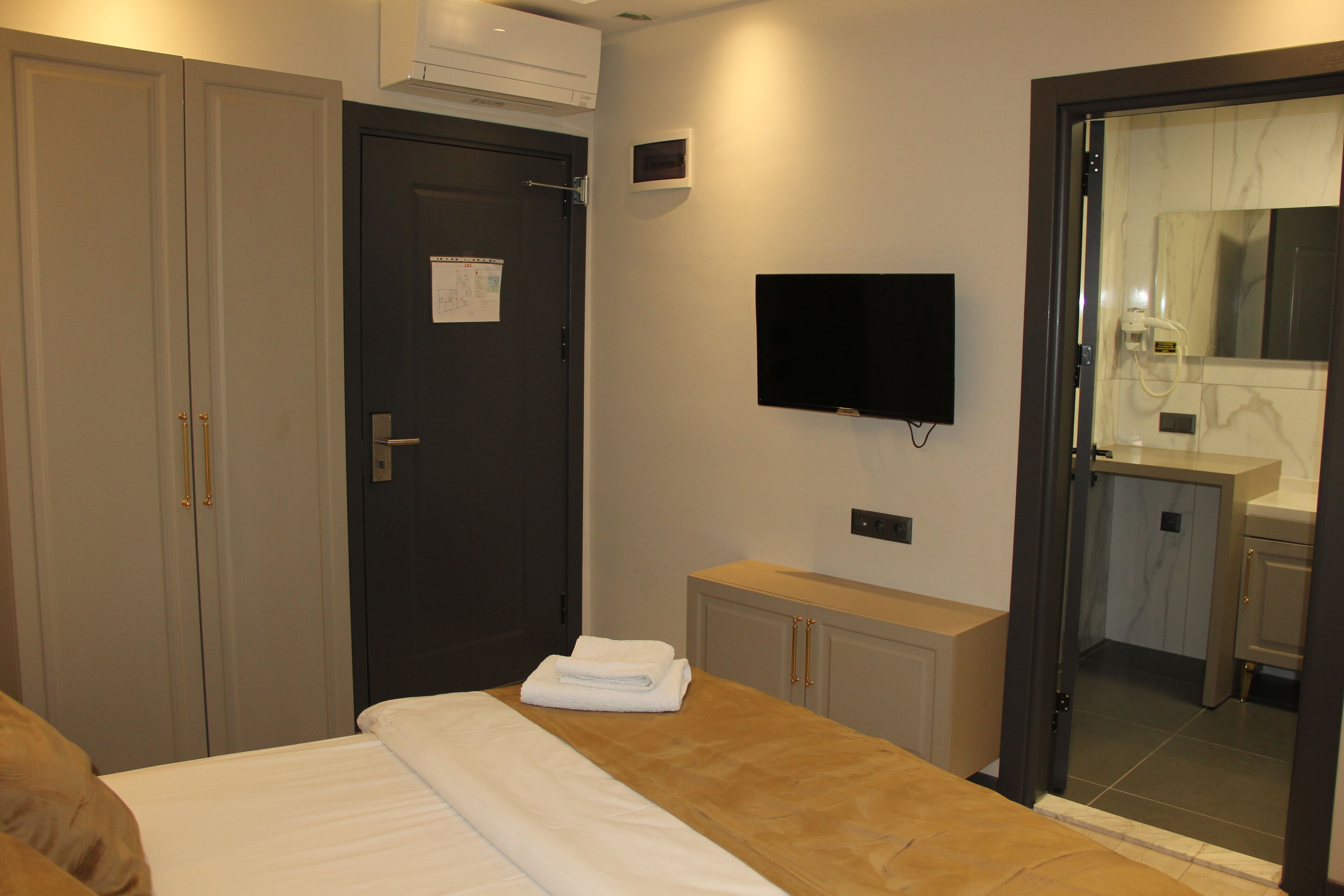 A hotel room with a bed, a TV mounted on the wall, a door with a notice, and a view into the bathroom.