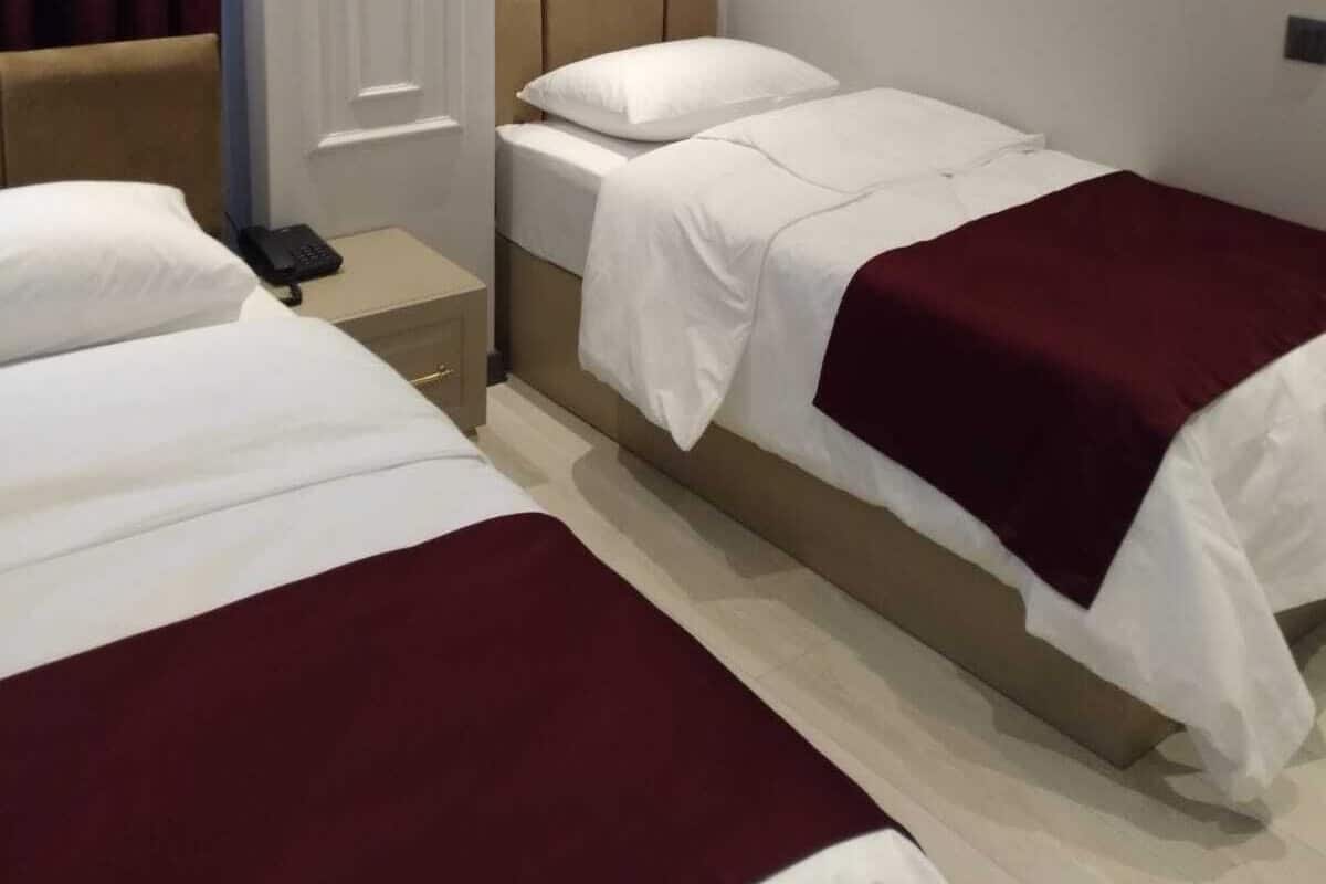 A hotel room with two single beds, a bedside table with a phone, a headboard, and an air conditioning unit on the wall.