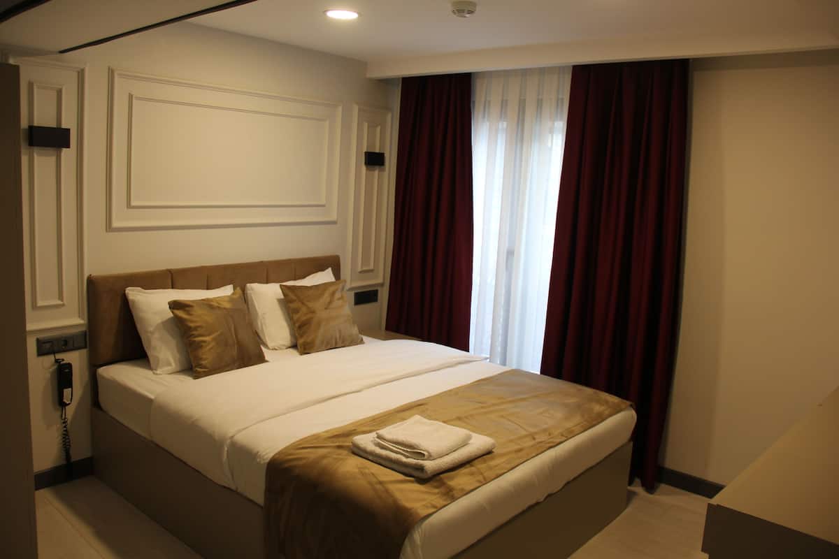 A hotel room with a large bed, a bedside telephone, and a window with curtains.