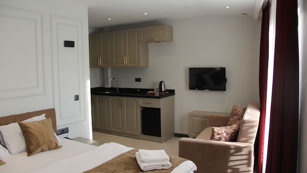 A hotel room with a bed, a sofa, a TV, a kitchen area, and a window with curtains. - EyüpSultan Palace Hotel (Eyup)