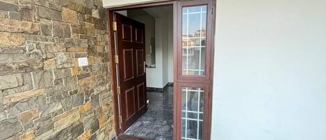 Una entrada con pared de piedra que conduce a un espacio con puerta de madera y panel de vidrio.