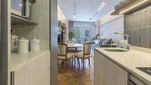 A modern kitchen with wooden cabinets, a dining area with chairs, and a view of the living room. - Renovated 2BR in Recoleta | Balcony & Smart Lock (Recoleta)