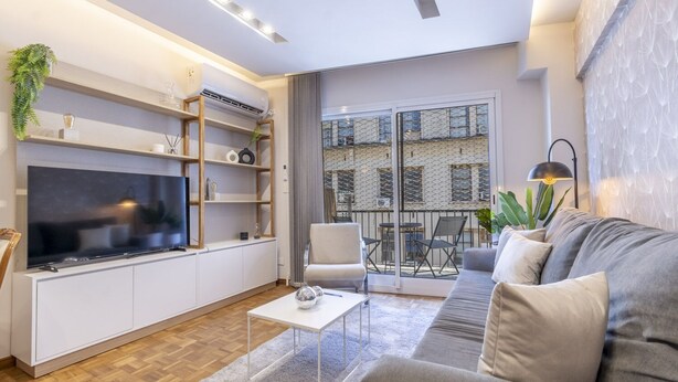 A modern living room with a flat-screen TV, built-in shelves, a sofa, and a balcony with a view of the city. - Renovated 2BR in Recoleta | Balcony & Smart Lock (Recoleta)