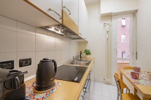 A compact kitchen with a built-in stove, a coffee maker, and a window overlooking a red brick building. - BnButler - Mussi, 10 (Milano)