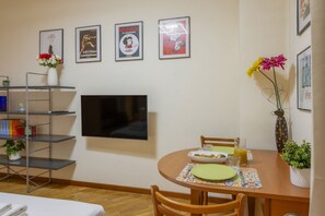 Een eetgedeelte met een ronde tafel, stoelen, een flatscreen-tv en lijstjes met posters aan de muur.