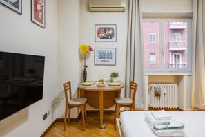 Hotelkamer met een bed, een televisie, een eettafel met stoelen, een bloevas en afbeeldingen in lijsten aan de muur.