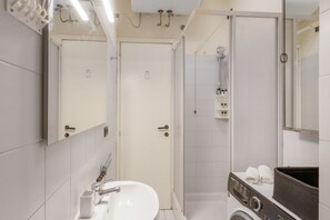 Een moderne badkamer met een wastafel, spiegel, douche en een wasmachine.