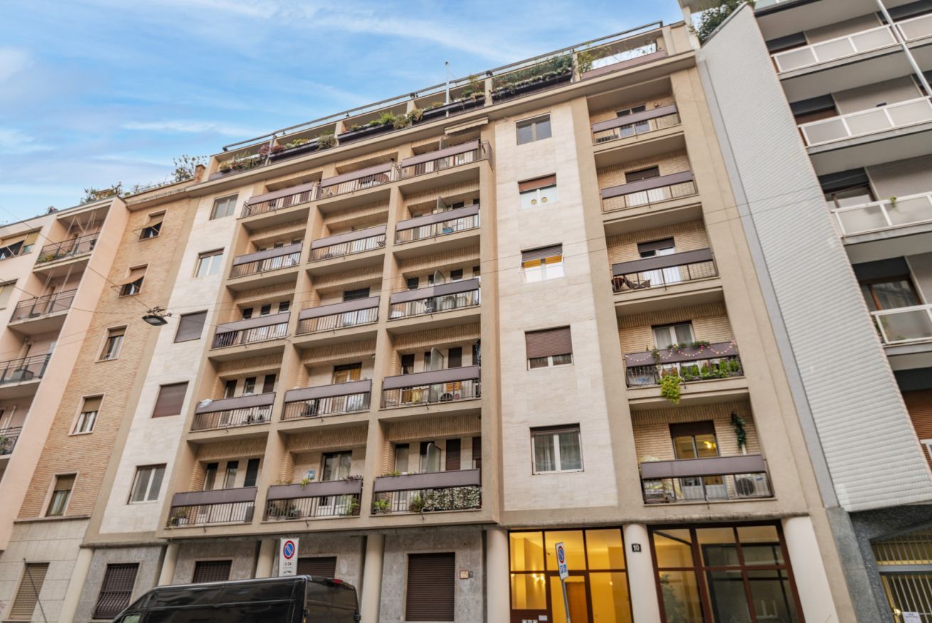 Un immeuble résidentiel à plusieurs étages, doté de balcons, d’une entrée au rez-de-chaussée et d’un panneau bien visible indiquant qu’il est interdit de se garer.