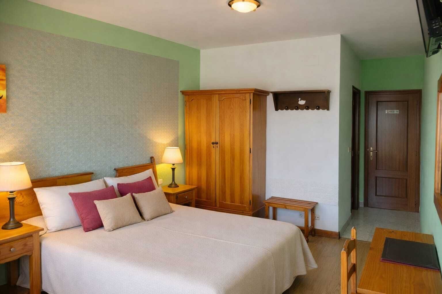 Una habitación de hotel con una cama, mesitas de noche, un armario, una pequeña mesa y una silla.