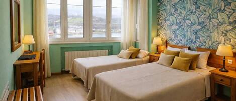 Une chambre d’hôtel avec deux lits, un bureau, une chaise, un radiateur et une fenêtre donnant sur un beau paysage.