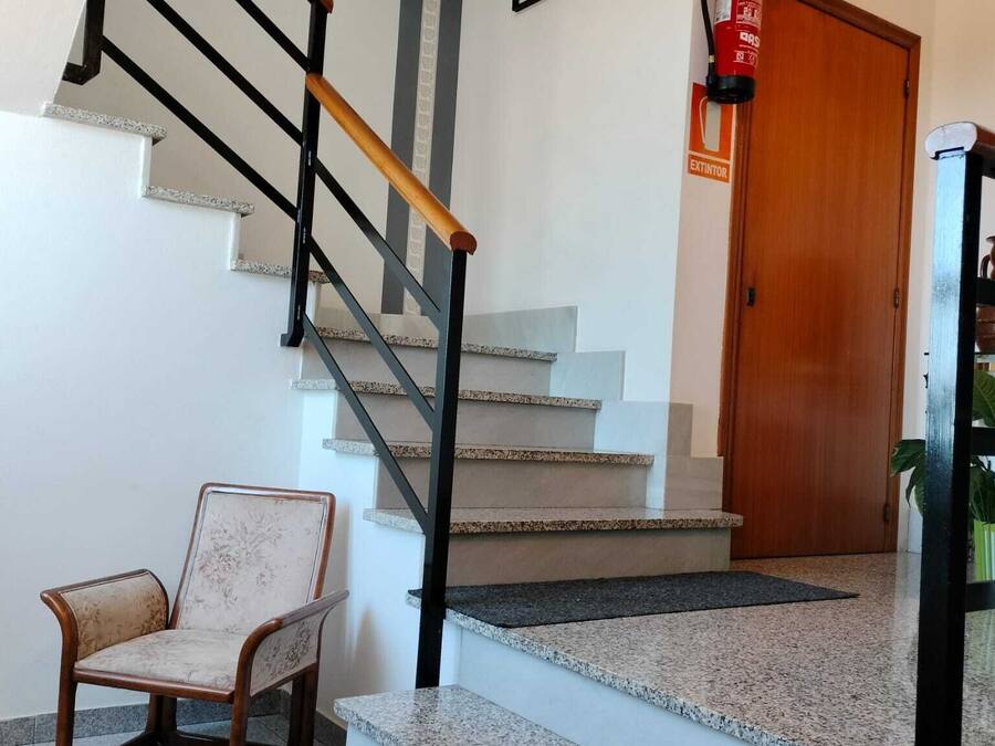 A staircase with a wooden handrail and a chair near the bottom.