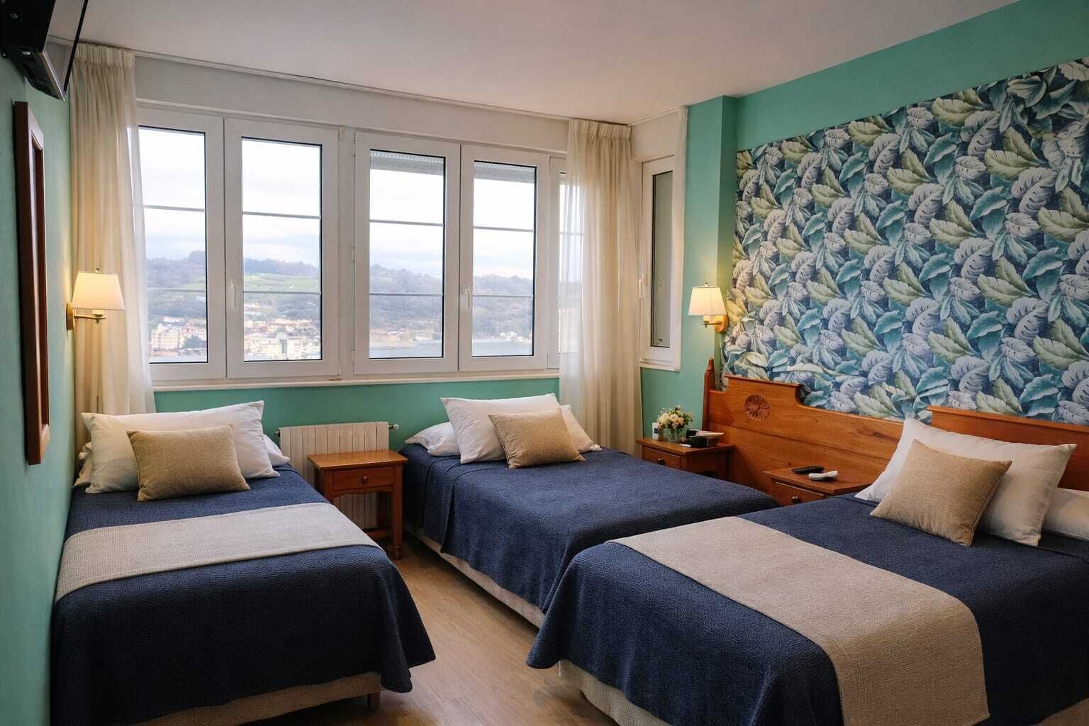 A hotel room with two beds, a large window with a view, and a floral wallpaper.