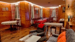 Un acogedor interior de cabaña con paredes de madera, una zona de comedor con mesas y sillas, y un espacio de descanso con sofá y sillón.