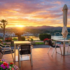 An outdoor patio with a table and chairs, overlooking a river and a bridge.