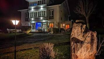 Un bâtiment à deux étages doté d’une entrée bien éclairée et d’un grand élément décoratif en roche au premier plan.
