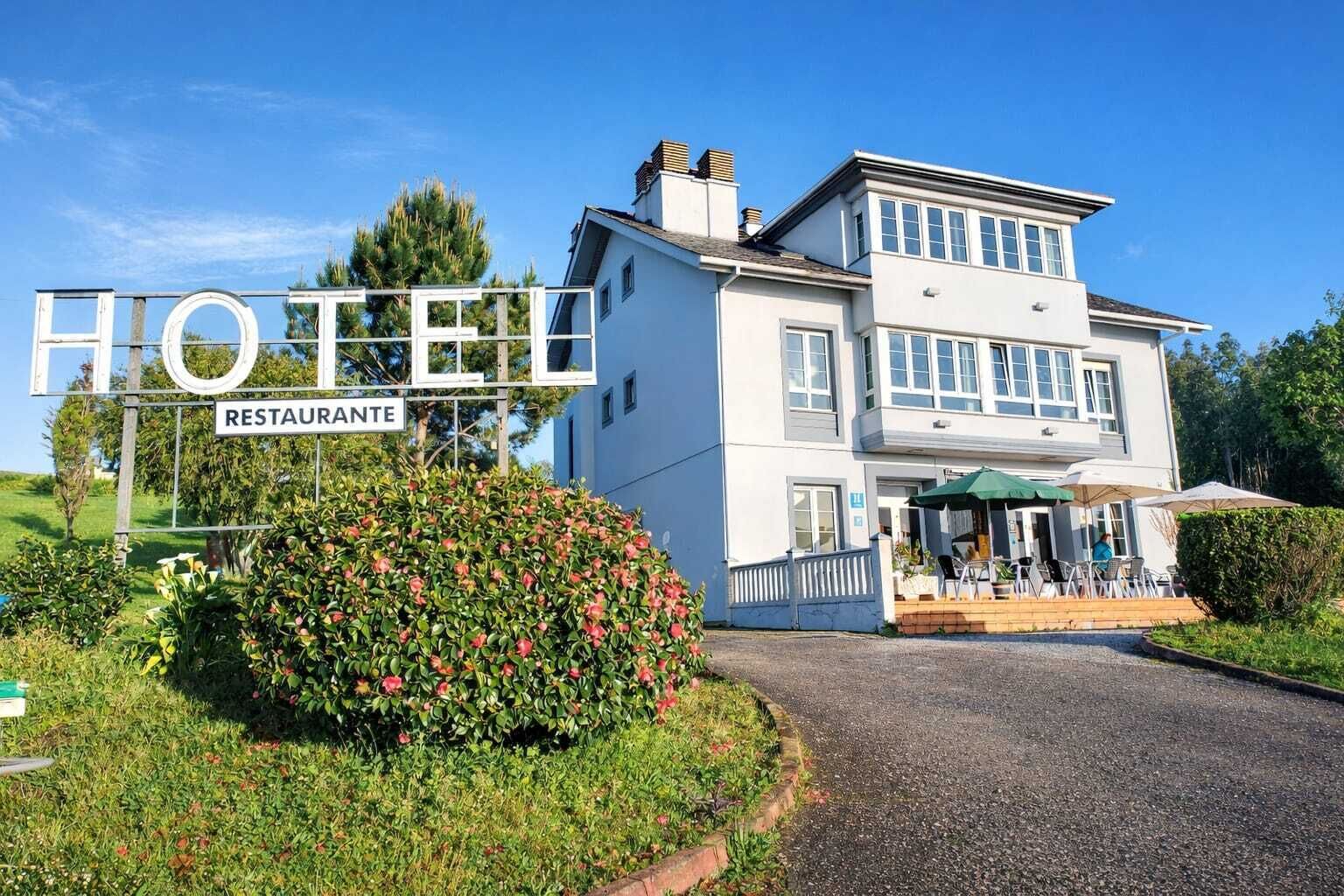 Un hotel con un letrero que indica que alberga un restaurante, un jardín bien cuidado y una entrada acogedora con mesas al aire libre.