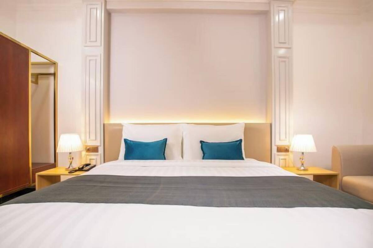 Ein Hotelzimmer mit einem großen Bett, zwei Nachttischen mit Lampen, einem Sessel und einem Spiegel.