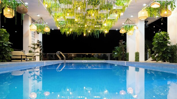 A pool with hanging plants and lights, surrounded by columns and a clear night sky.
