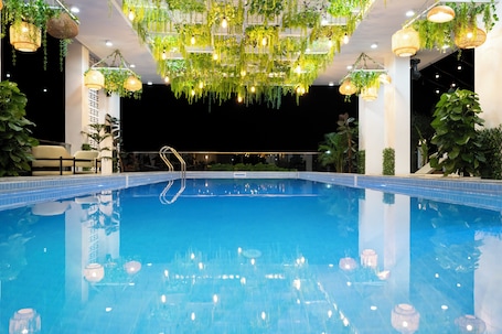 A pool with hanging plants and lights, surrounded by columns and a clear night sky.. Cambana Poipet Hotel