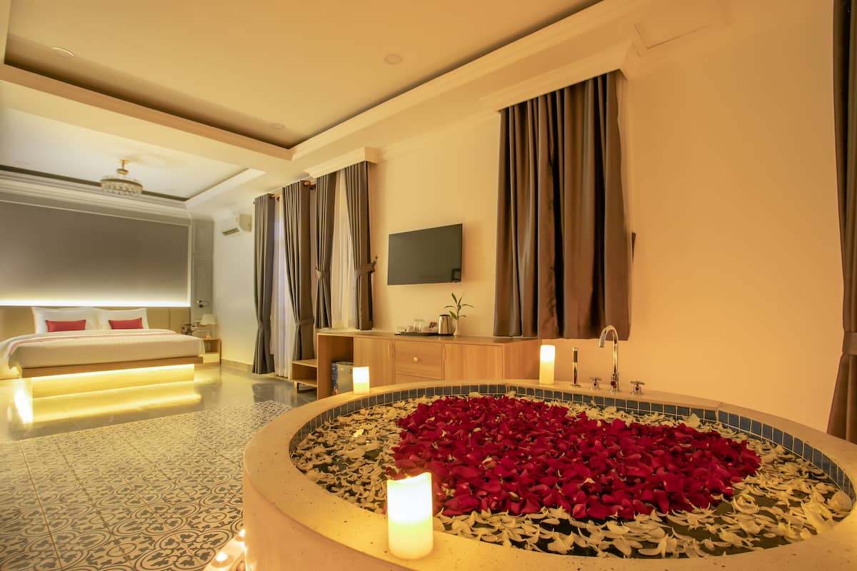 Ein Hotelzimmer mit Bett, einem Badezimmer mit einer Badewanne voller Rosenblätter und einem an der Wand montierten Fernseher.