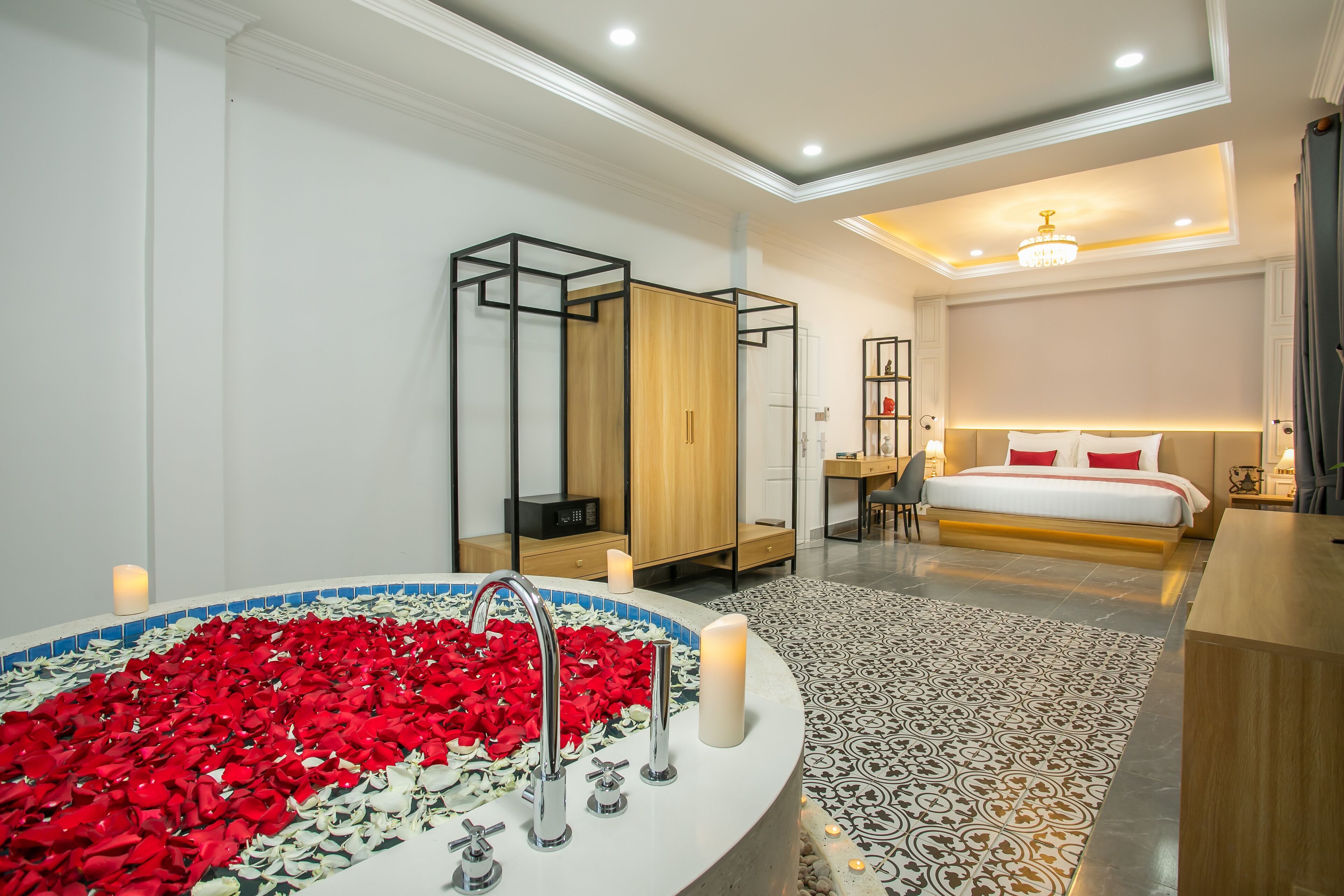 A modern bedroom with a large bed, a built-in desk, and a bathtub filled with rose petals.