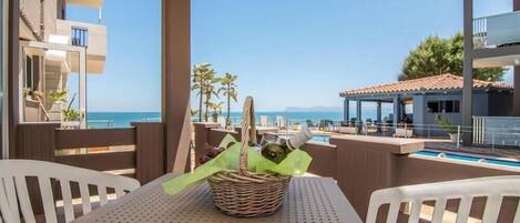 A balcony with a table and chairs, overlooking a pool and the sea.