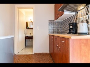 A compact kitchen with wooden cabinets, a tiled backsplash, and a coffee maker on the counter. - Room in Guest Room - Girogiali Beach Hotel (Chania)