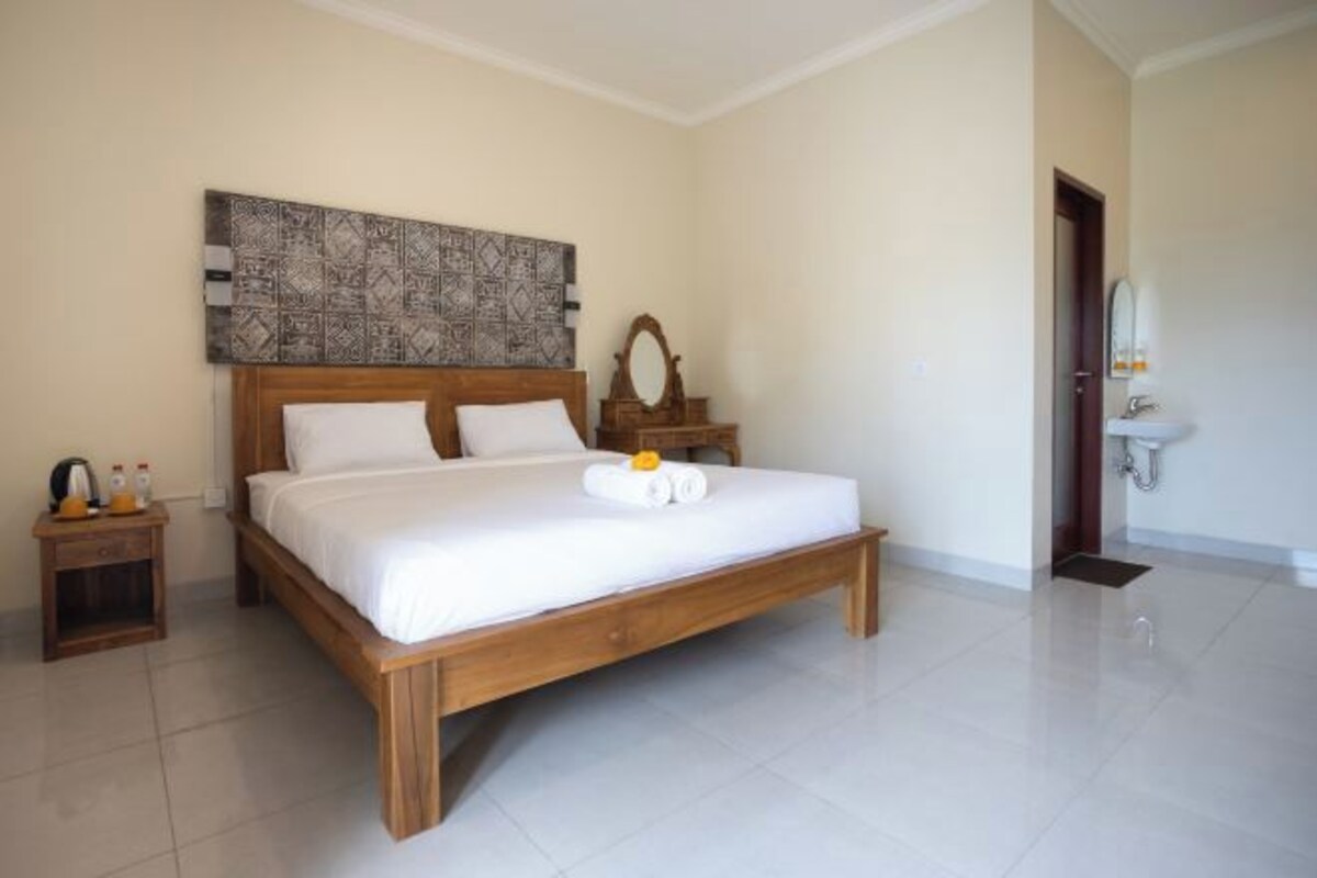 Un dormitorio con cama de madera, mesita de noche con artículos de aseo, espejo y baño con lavamanos y espejo.