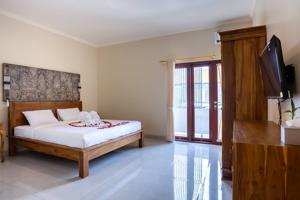 A bedroom with a wooden bed, a flat-screen TV, and a large window with curtains.