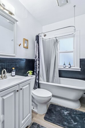 A bathroom with a white sink, toilet, and bathtub. There is a window above the bathtub, and a shower curtain is hanging over the tub.