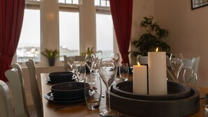 Una mesa de comedor dispuesta con platos, vasos y velas, con vistas al mar a través de amplias ventanas.