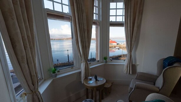 Una habitación acogedora con vistas al mar, que incluye una mesa redonda, dos sillas y un taburete pequeño.