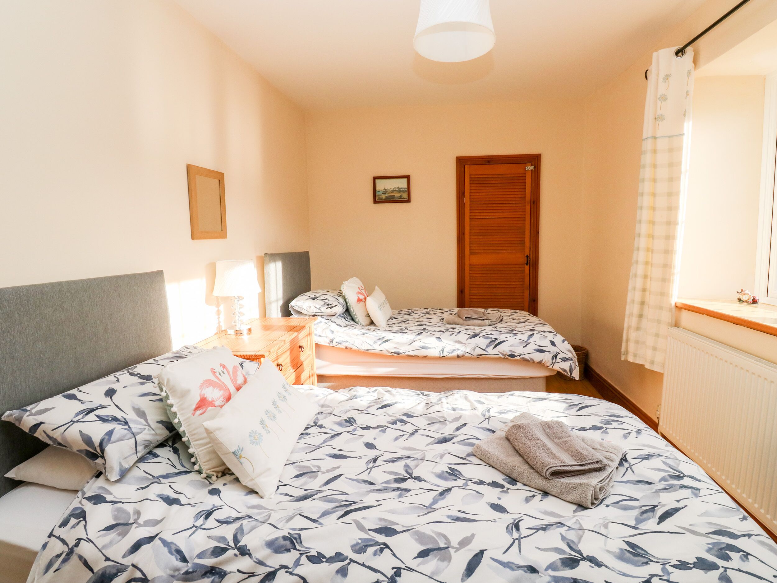 Un dormitorio con dos camas, un armario de madera, una mesita de noche con lámpara y una ventana con cortina.