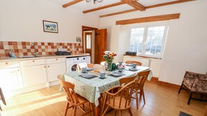 A kitchen with a dining table set for four, wooden chairs, a washing machine, and a window with a view. - Twyford Farm Cottage (Tiverton)