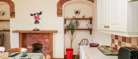 A cozy kitchen with a brick fireplace, wooden beams, white cabinets, and a dining area with a table set for two.