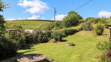 A wooden picnic table and benches in a grassy outdoor area with a clear sky and hills in the background.