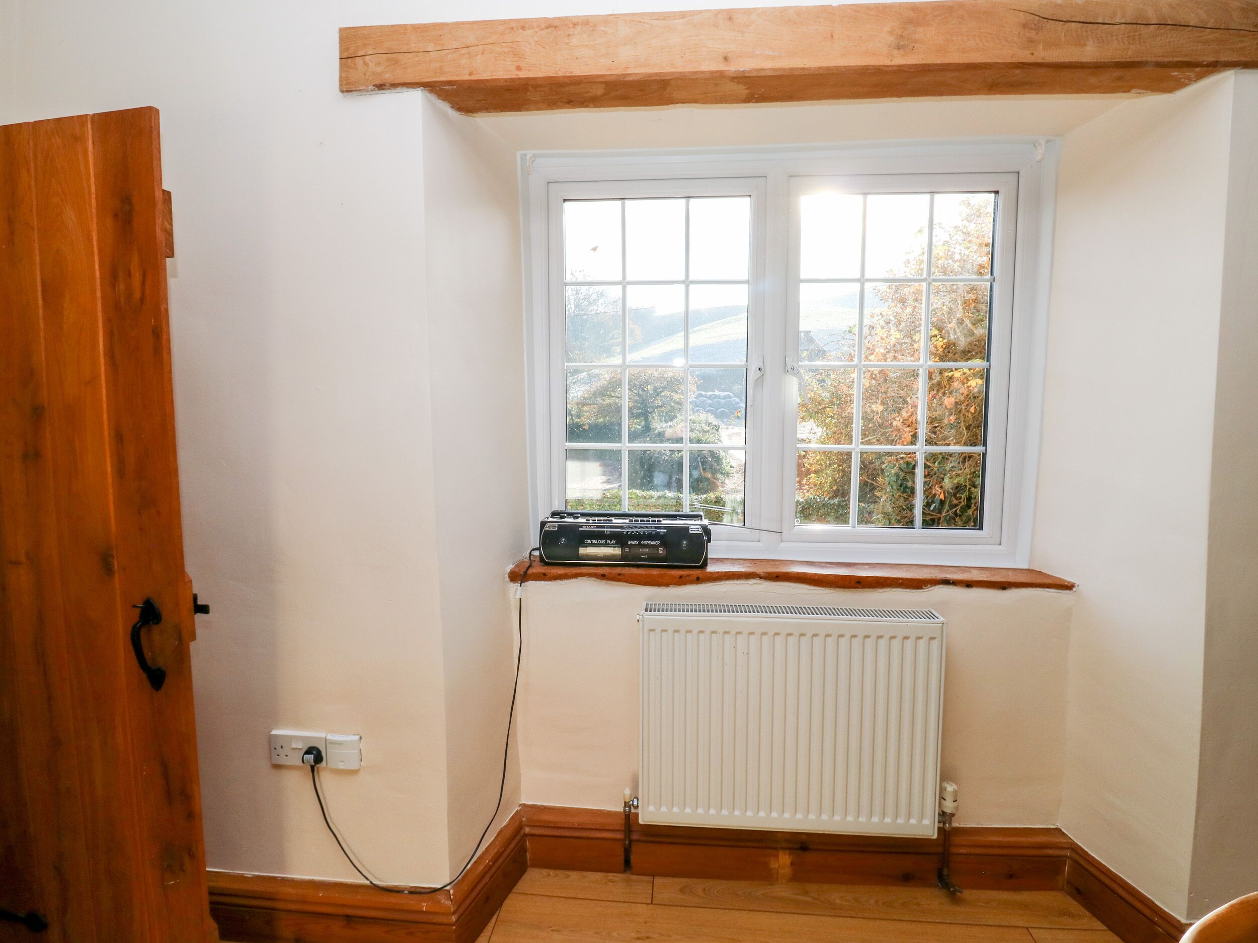A corner room with a window, radiator, and wooden beam ceiling.