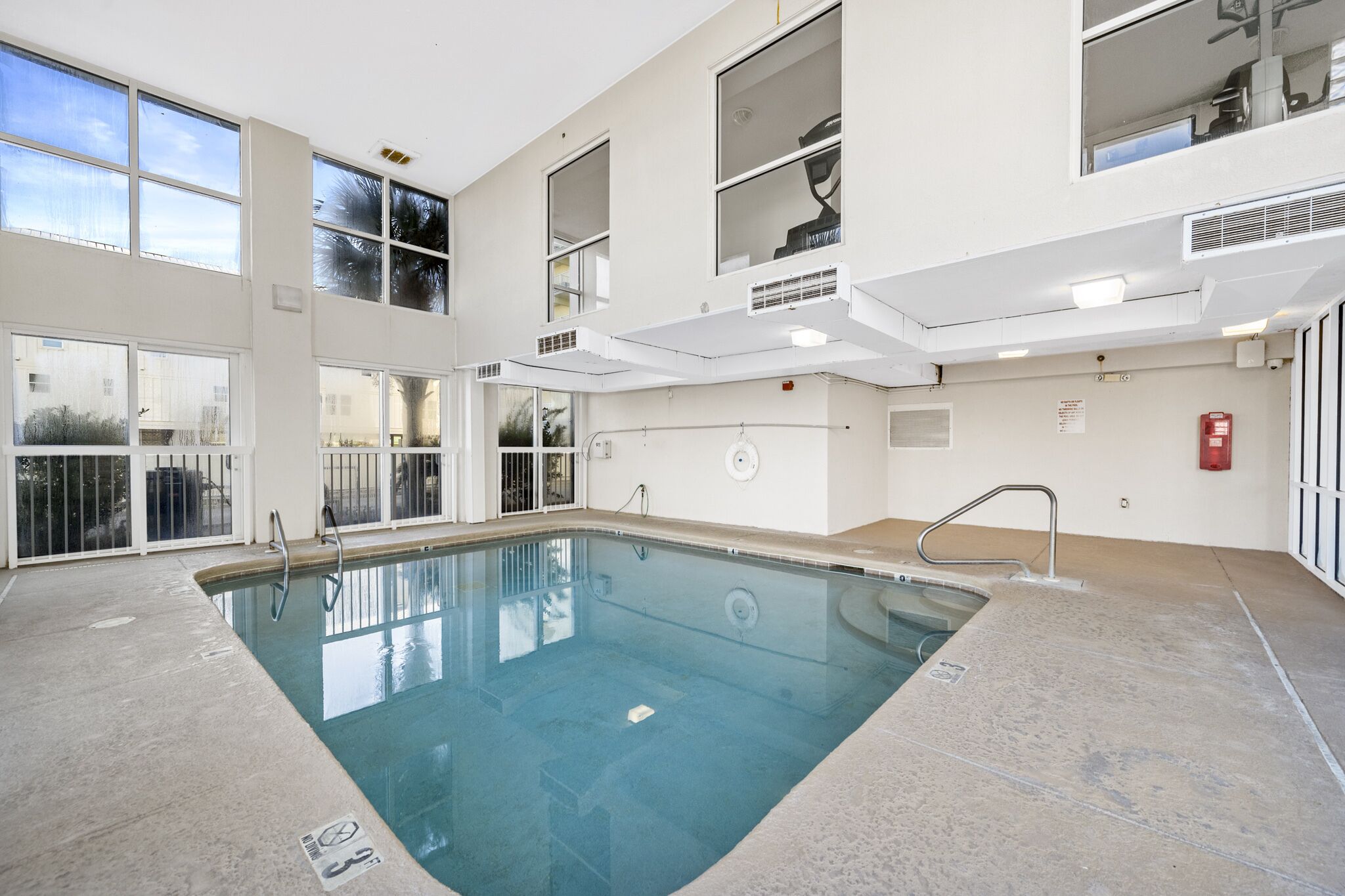 An indoor swimming pool with clear glass walls, a concrete floor, and a metal ladder.