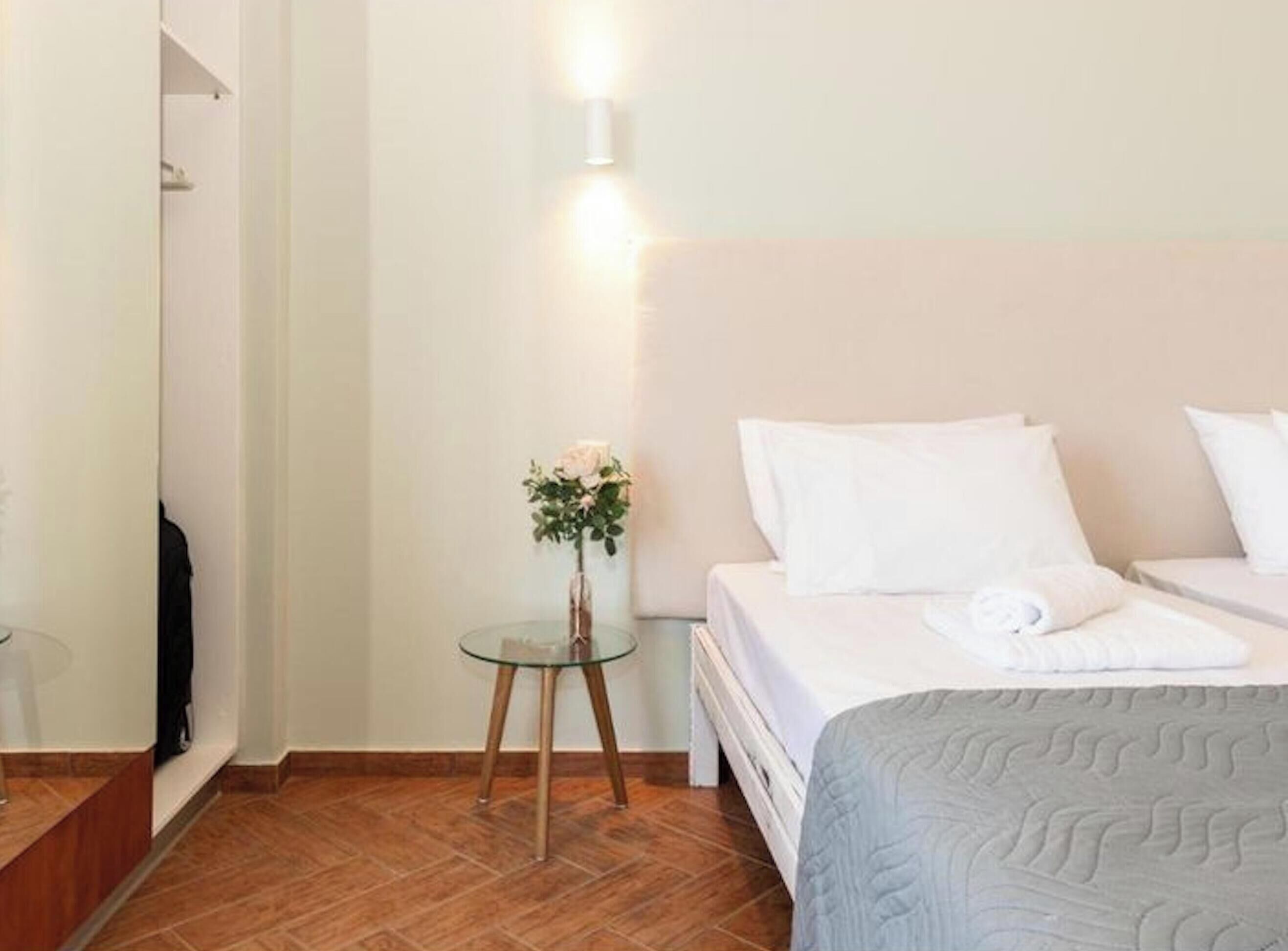 A hotel room with a bed, a small table with a vase of flowers, and a wall-mounted light.